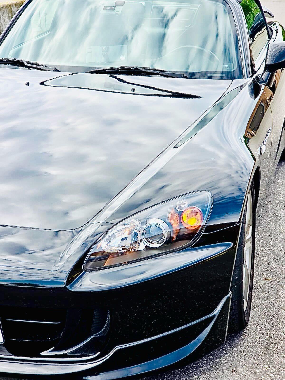 Black Honda S2000 hood and headlight after paint correction and ceramic coating, reflecting the sky
